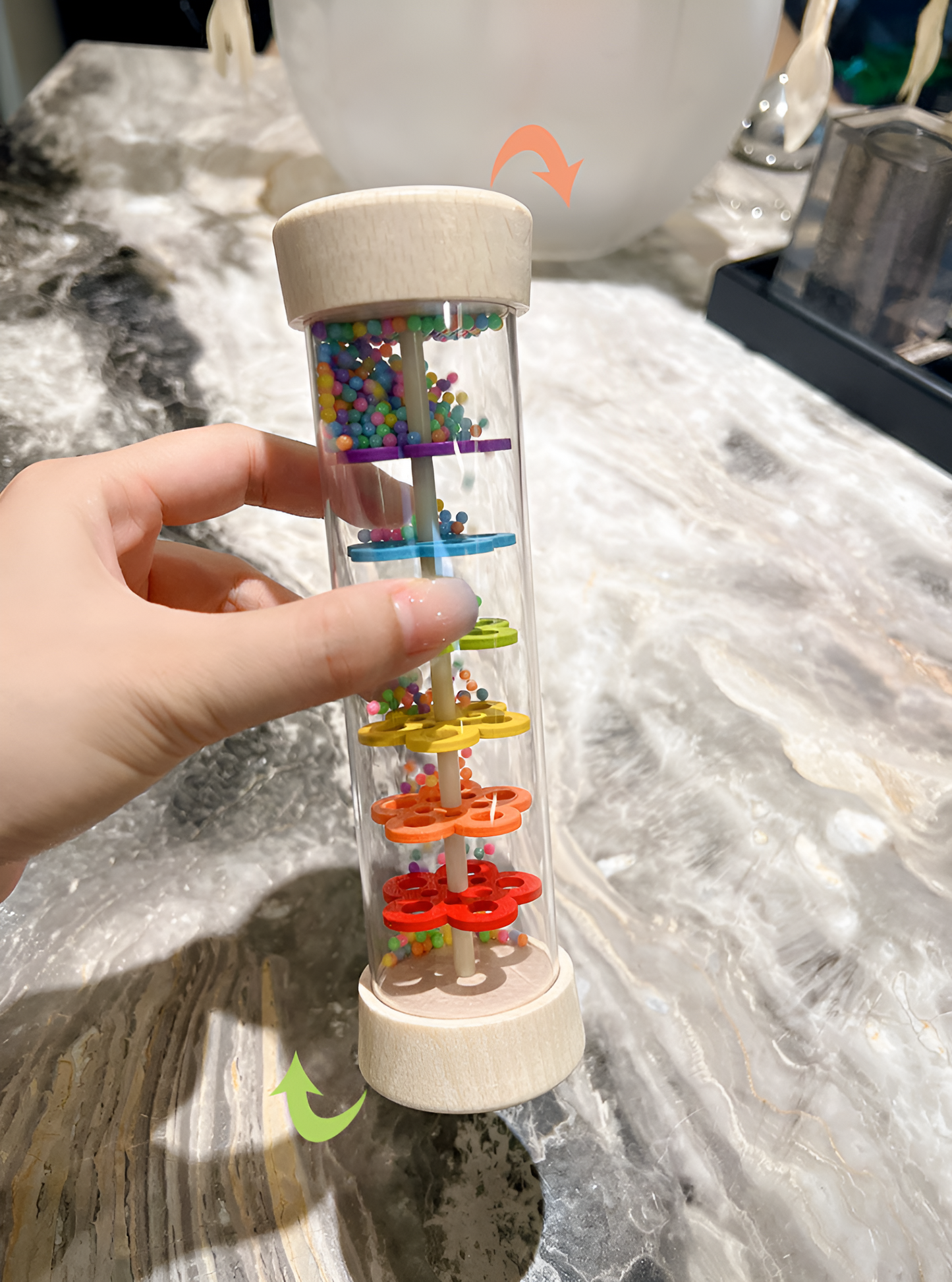 Hand demonstrating the use of a Montessori Wooden Toddler Rattle, featuring colorful gears and beads that encourage sensory play, fine motor skills, and auditory development.