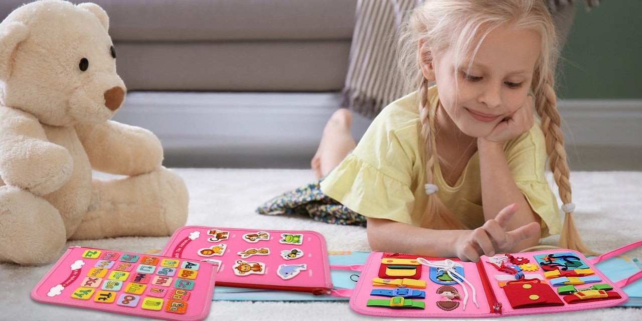 Young girl playing with pink Montessori busy board upgraded edition on floor, foldable felt activity board with multiple learning panels, fine motor skills and sensory toy for toddlers aged 18 months and up.