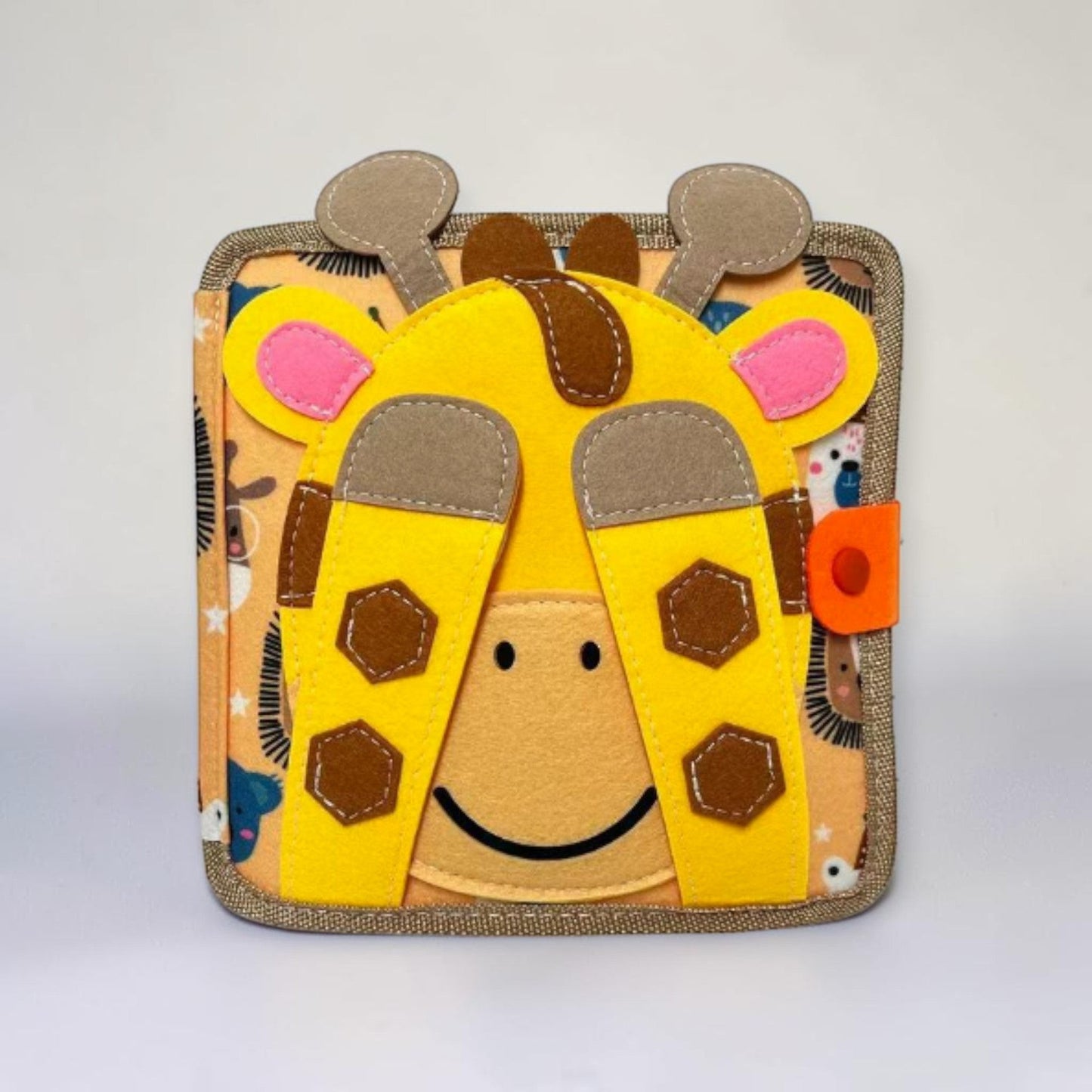 Montessori busy board quiet book giraffe edition, yellow and brown felt animal book with smiling giraffe face and snap closure on cover, sensory activity book for toddlers and preschoolers aged 12 months and up.